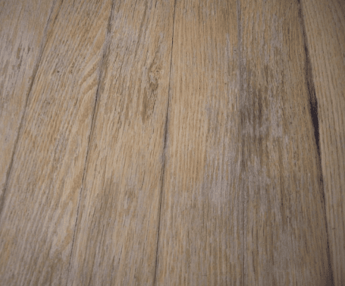 Water-damaged timber floorboards showing patches of discolouration and fading.