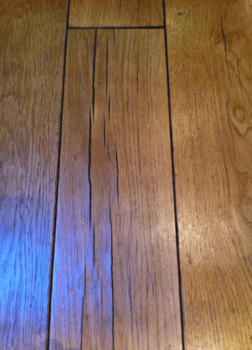 Wooden floorboards splitting and separating along the edges due to water exposure.