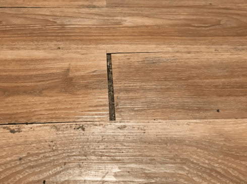 Floorboards with noticeable gaps and misalignment caused by prolonged water damage.